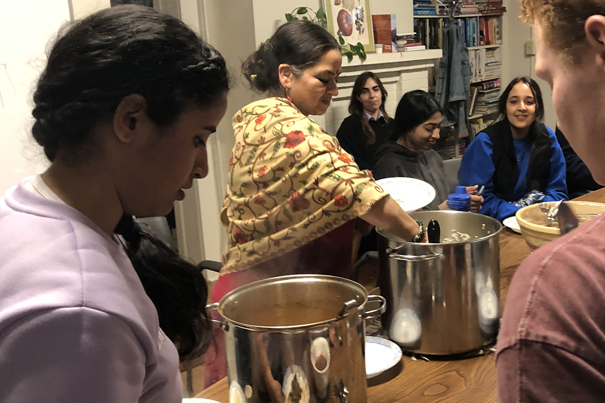 Kashika Singh reaching into a large steaming pot, surrounded by others people around a table