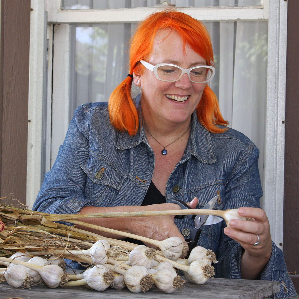 Kayte Young smiling while cutting a garlic stock, stitting at a table outdoors