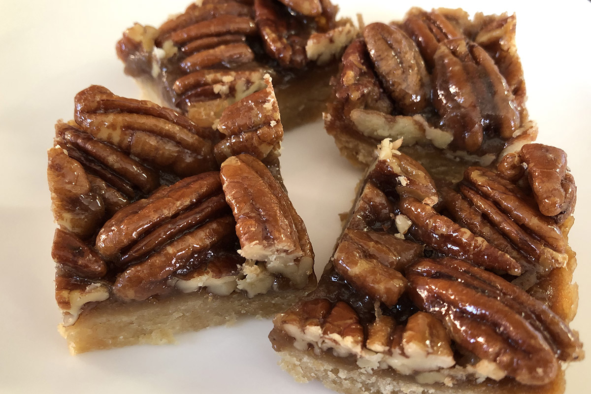 Four pecan bars arranged on a white plate.