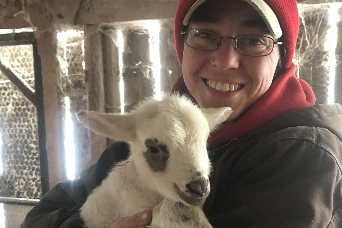 Liz Brownlee in winter clothes holding a baby lamb and smiling at the camera