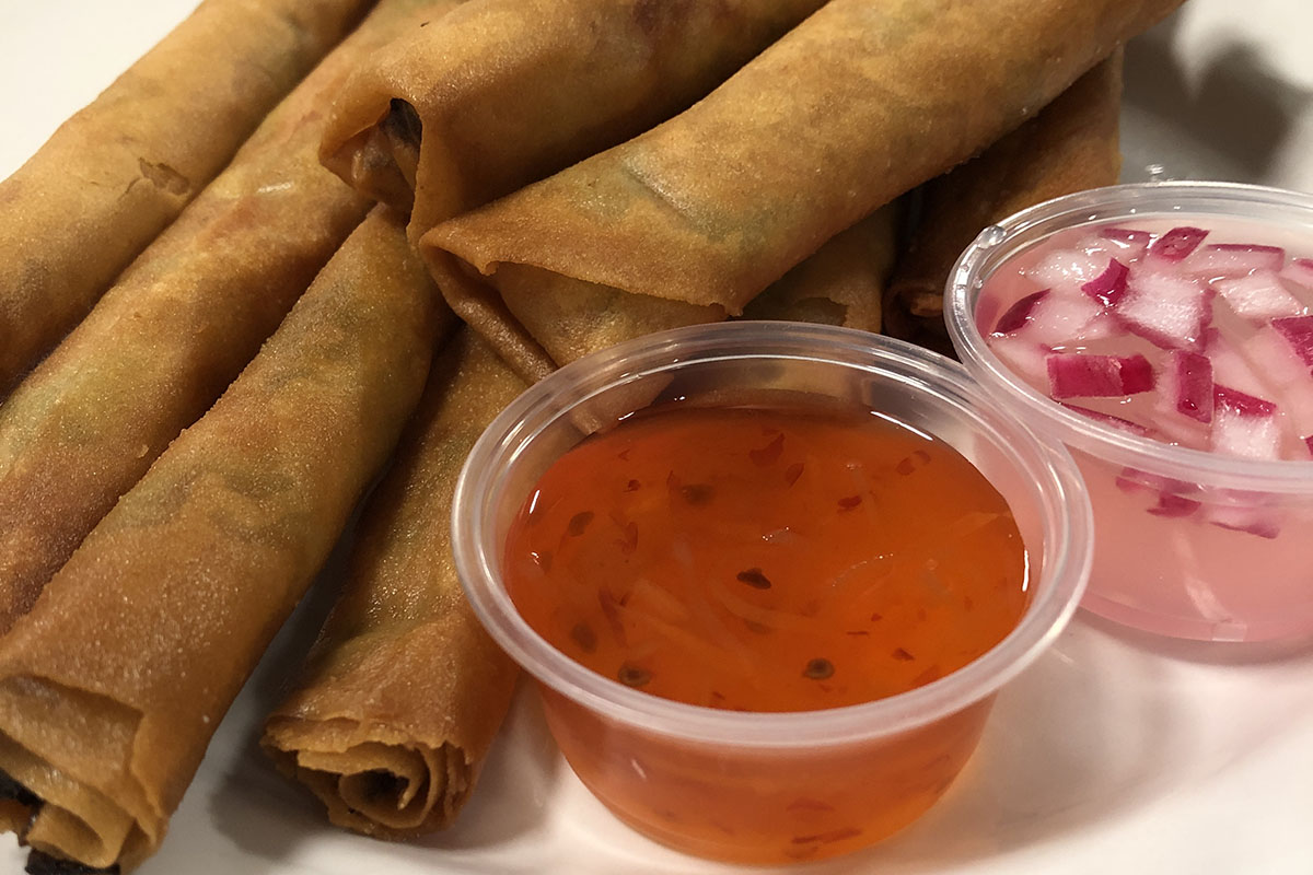 fried spring rolls on a plate with an orange sauce in a small container and a clear sauces with diced onions in a small container