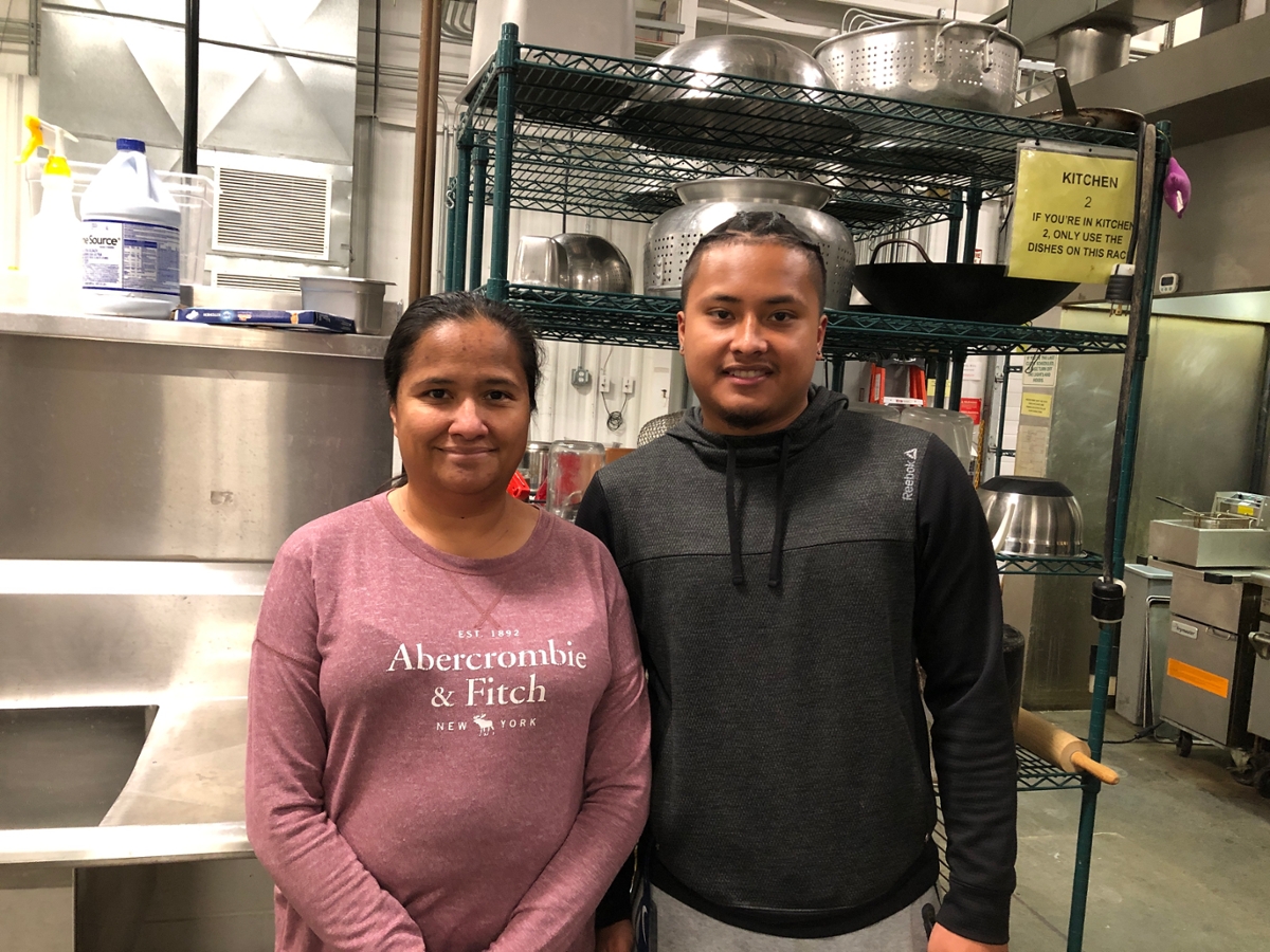 Maria St. Clair and Chris Manansala standing in a comercial kitchen with shelving behind them