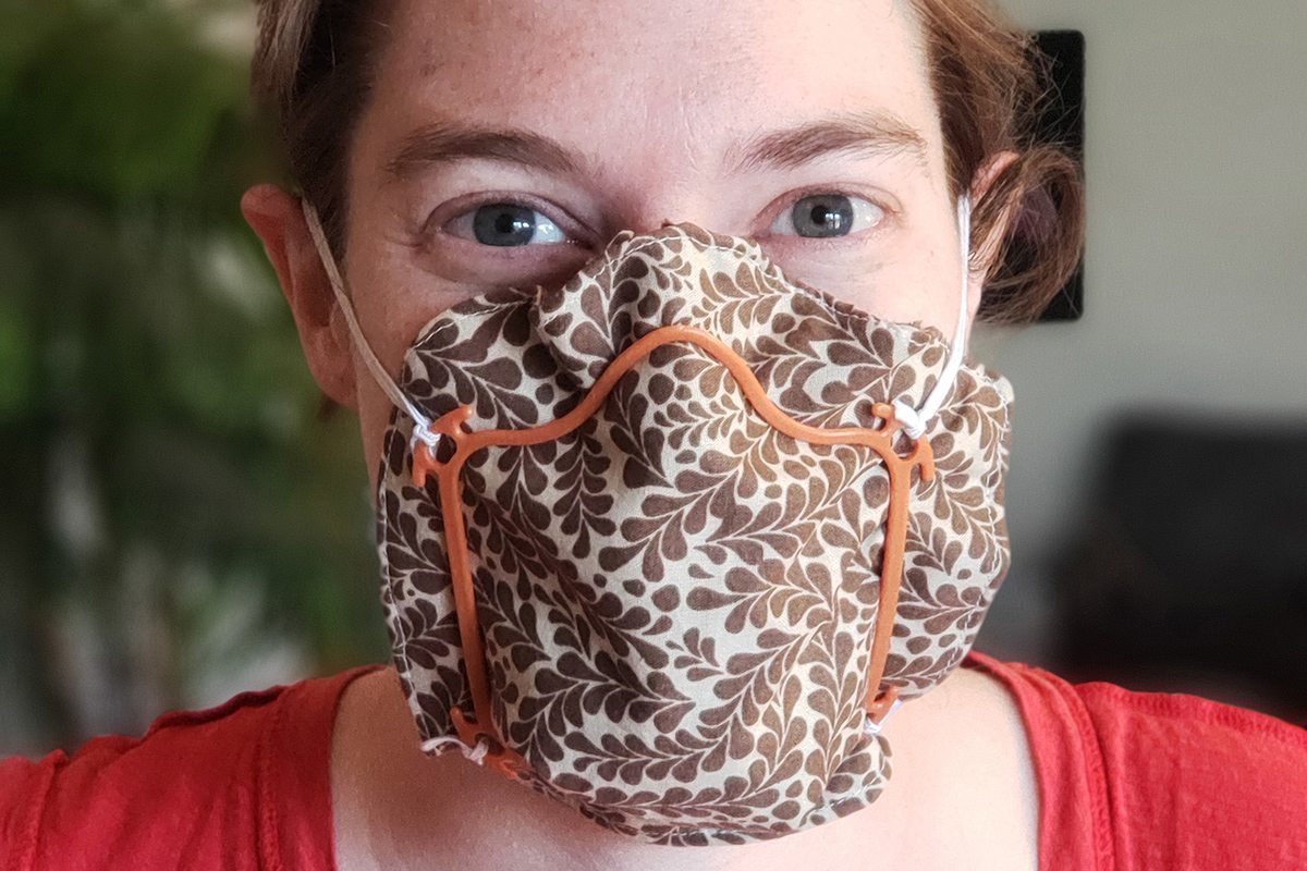 Close-up of a woman's face with patterned cloth and a mask frame over her mouth, nose and chin.