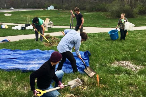 People working with shovels and tarps in a green field. 