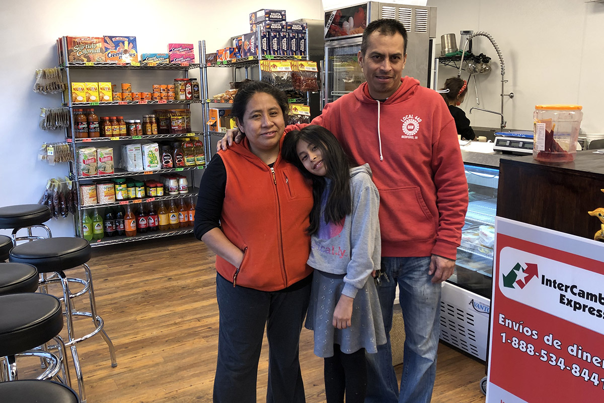 Pilar Gonzales with her husband and daughter standing in a small store with merchandise and barstools n background