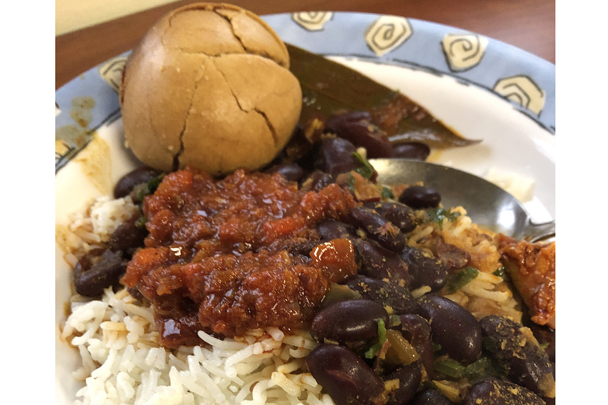 A close up of a plate of food with beans, rice, a bright red sauce and a round, cracked roll