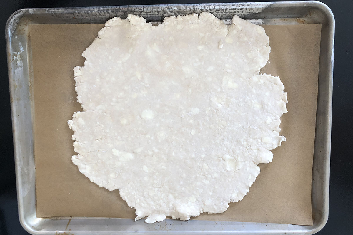 Pie pastry with rough edges rolled out and on brown parchment on a metal baking sheet.