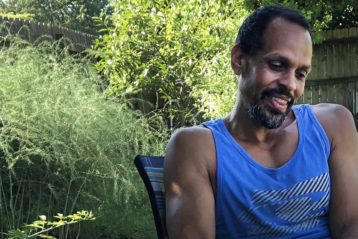 Ross Gay seated outside with greenery in background