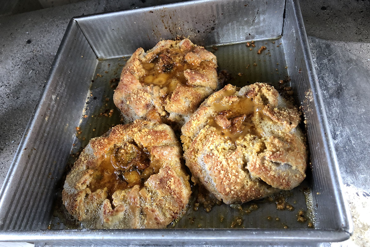 Three small, golden brown, rustic tarts with tomato filling and parmesan cheese in a metal pan.