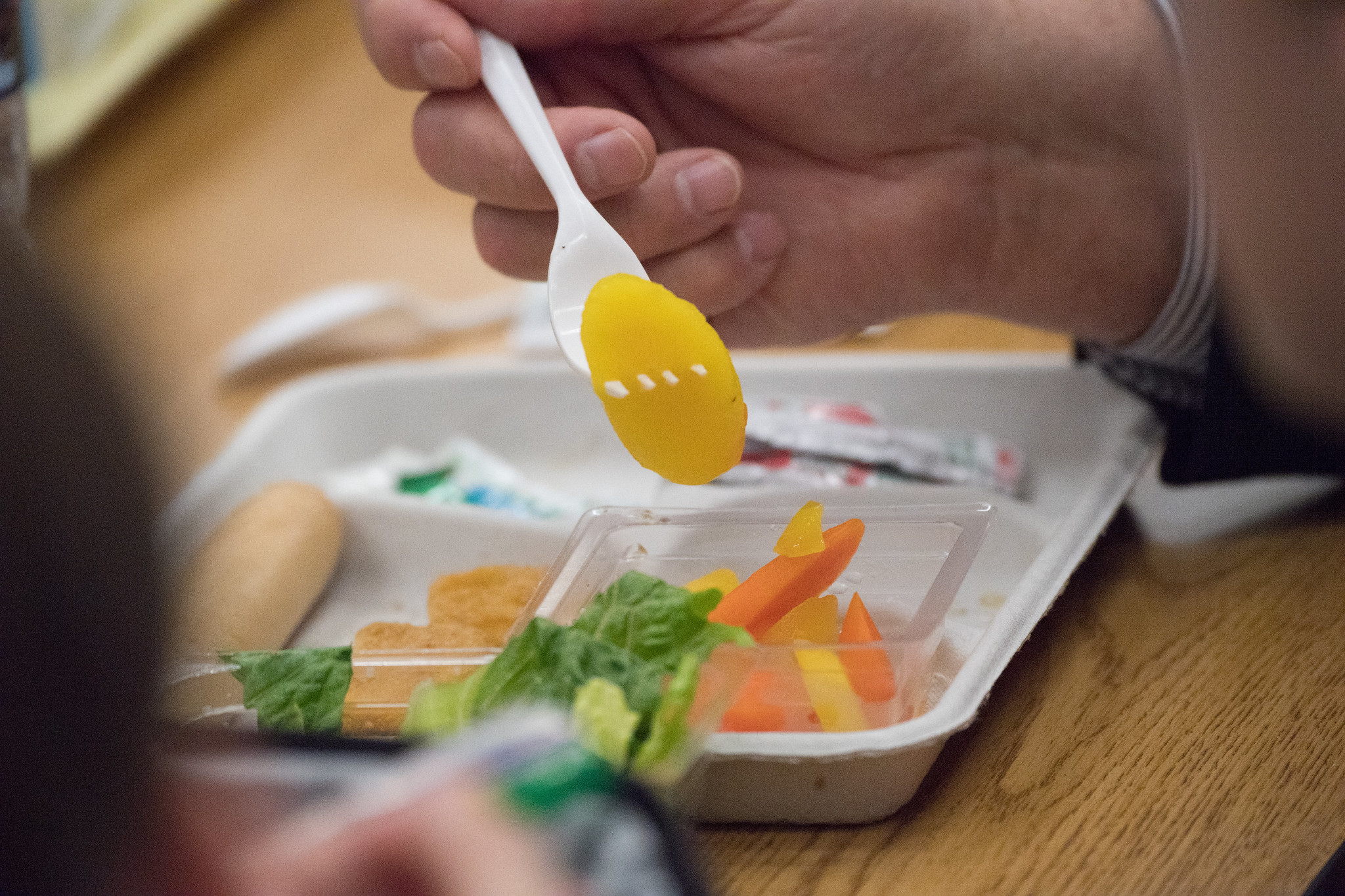 A hand holding a plastic spork with a piece of yellow pepper, from a pre-packaged meal
