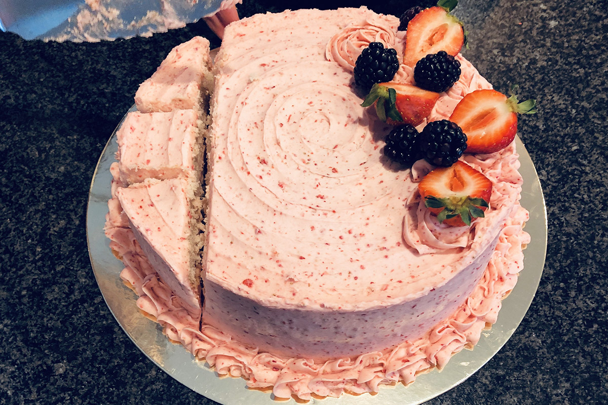 overhead view of a round, pink, decorated cake with one two-inch slice on one edge and that slice divided into 3 pieces 