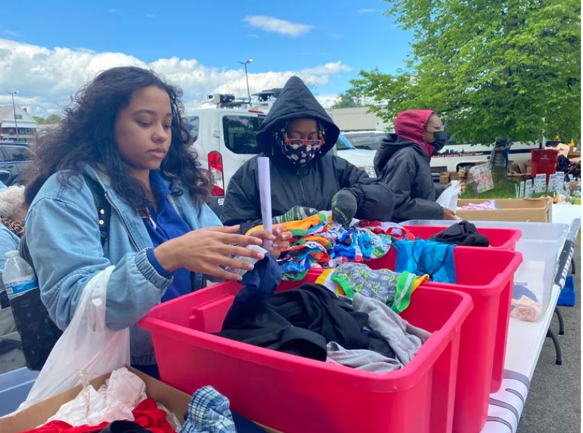 People sorting through bins of clothes on a table outdoors