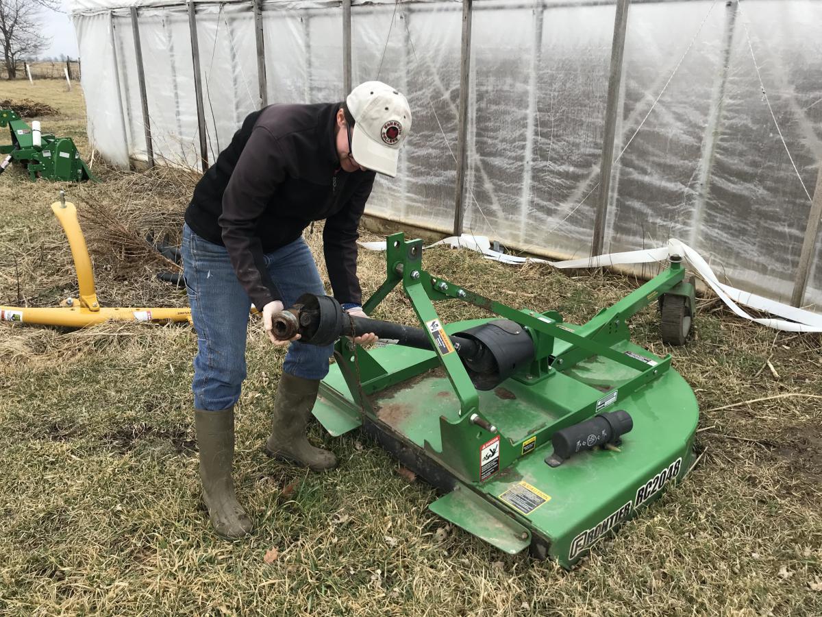 Dusty Spurgeon handling a part on a piece of farm equipment, with a hoophouse in the background