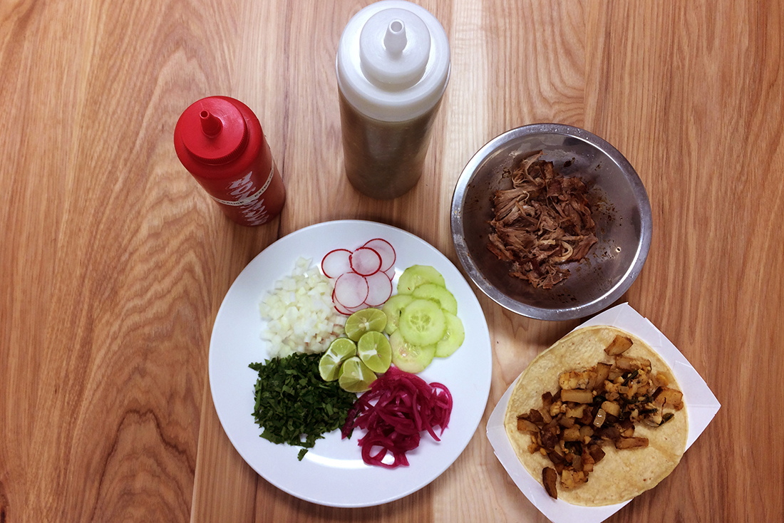 Colorful ingredients for tacos, arranged on a wooden table and white plate, photographed from above.