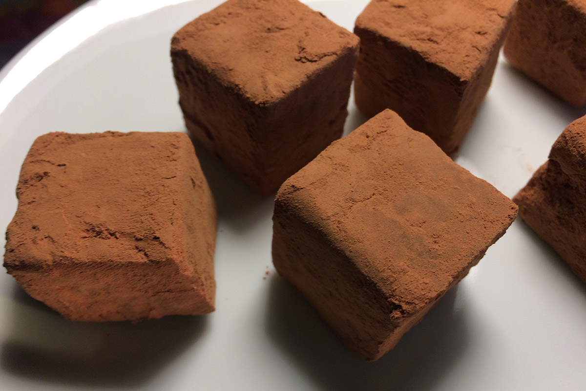 Cube-shaped chocolate truffles dusted in cocoa powder arranged on a white plate