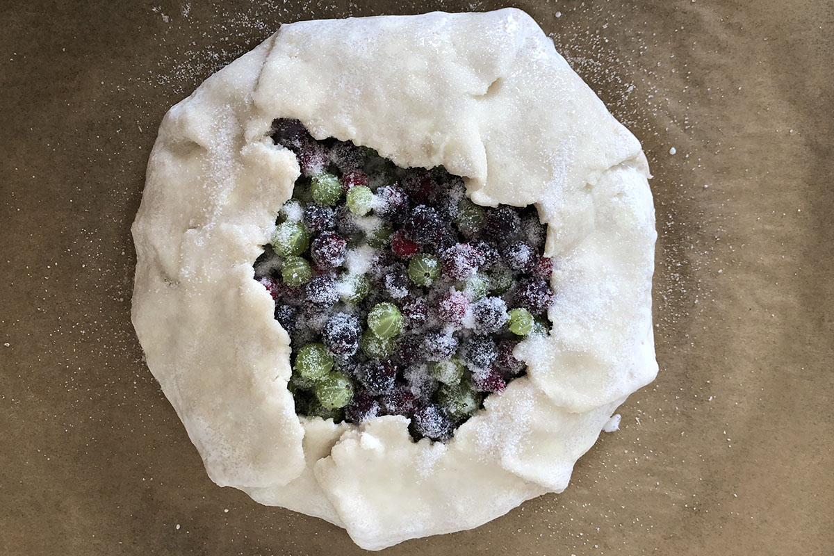 Roughly round-shaped unbaked pie pastry with berries inside.