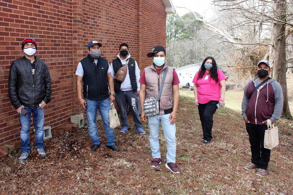 Six people wearing face masks standing outside next to a brick building. 
