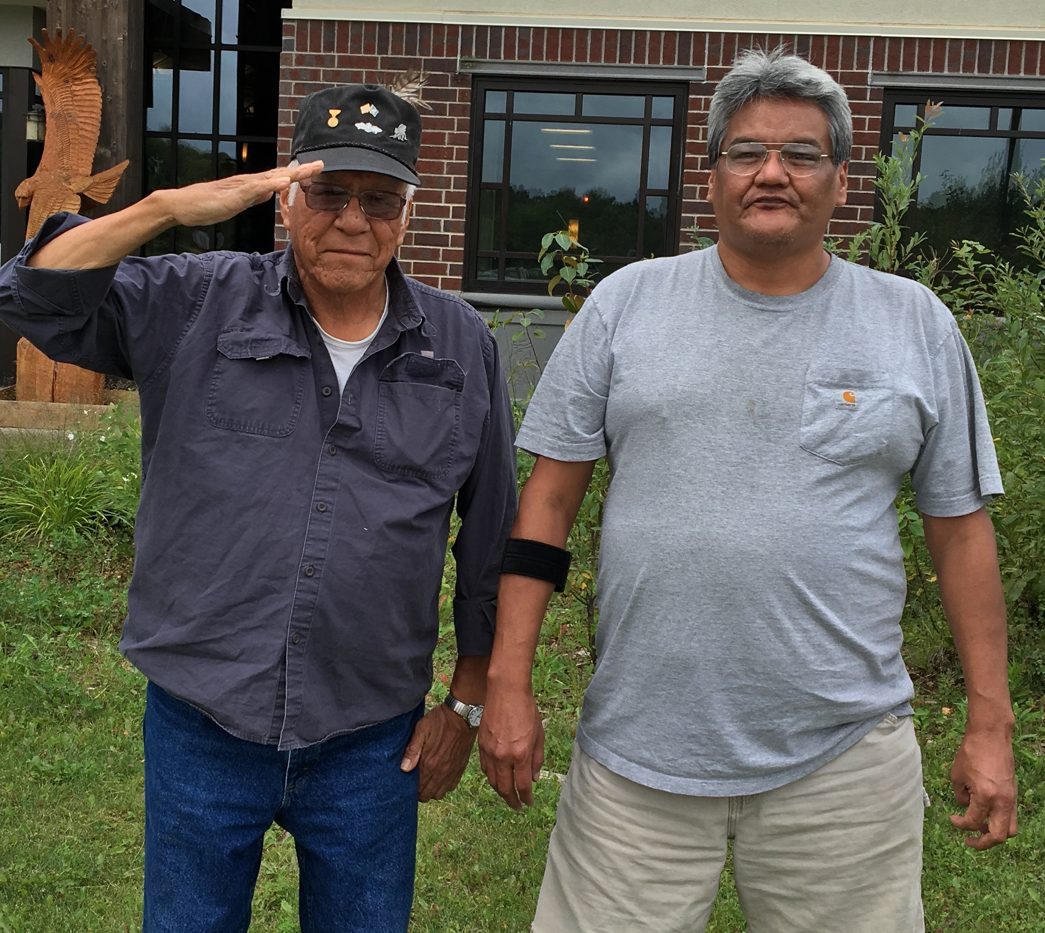 Gene Goodsky and Curt Goodsky standing outside, looking at camera. Gene's right hand is at his hat brim, in salute