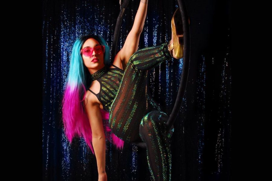 DJ Maddøg hangs off a metal ring while wearing a pink and blue wig.