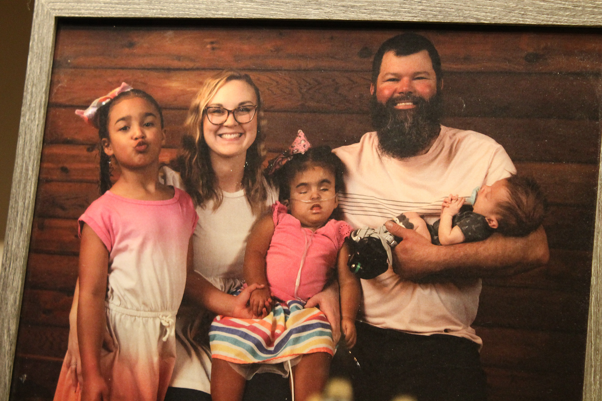 Christine and Luke Davis sitting for a family photo with their three children. The oldest child is standing next to Christine making a kissy face. Luke is holding the youngest child, who is an infant. Tala Beth Davis is in the center wearing oxygen p