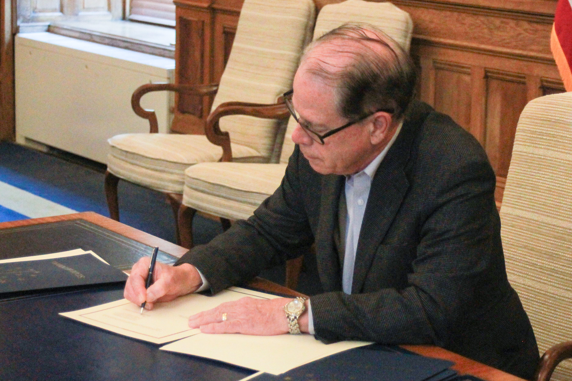 Mike Braun sits at a desk in his office, signing an executive order. 