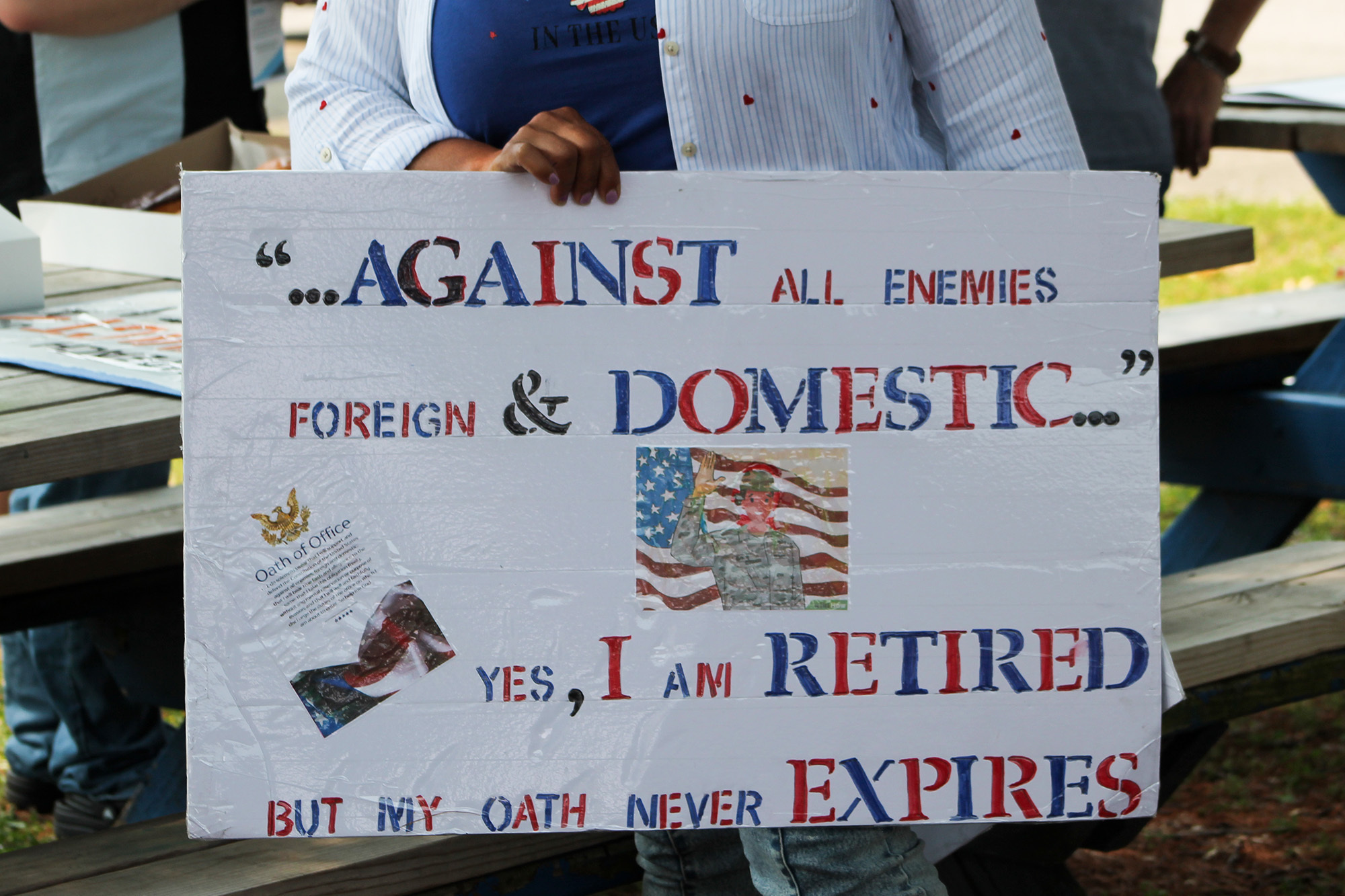 An army veteran holds a sign that says “‘Against all enemies foreign and domestic…’ Yes, I am retired but my oath never expires.”