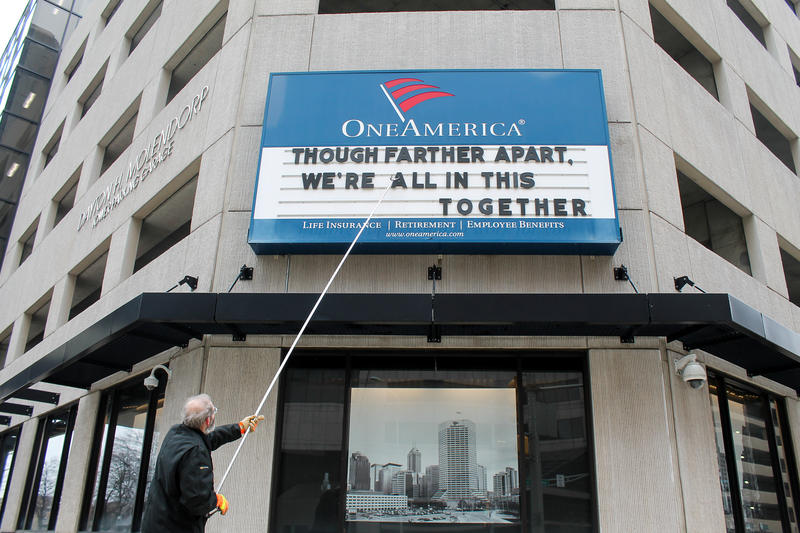 A man adjusts the One America sign in downtown Indianapolis. It usually displays a pun, but the message shortly before the governor's address reads: "Although father apart, we're all in this together."