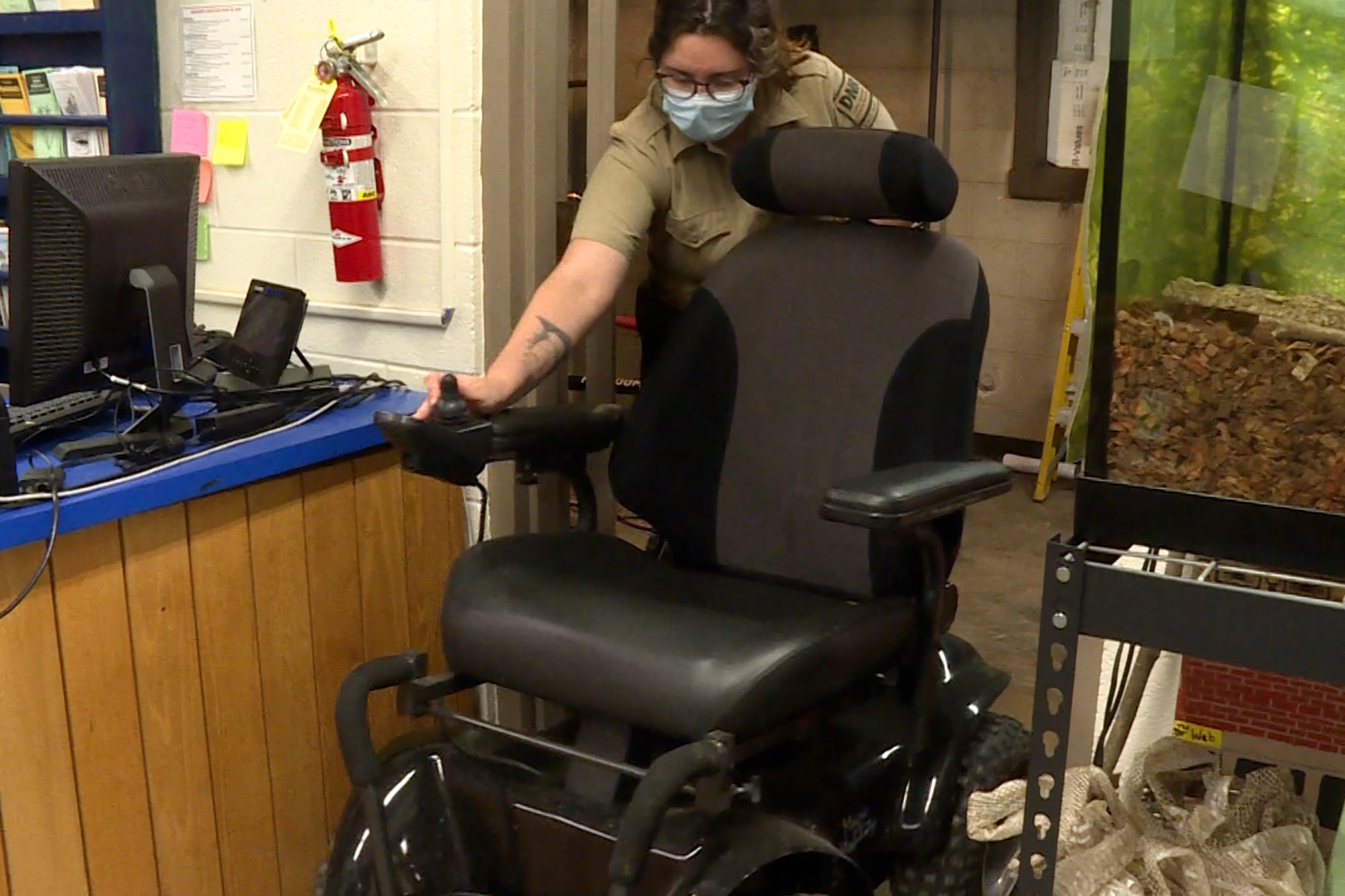 A DNR employee moves a motorized chair from a cramped closet. The chair has large wheels that look more like bike tires than typical wheelchair tires.