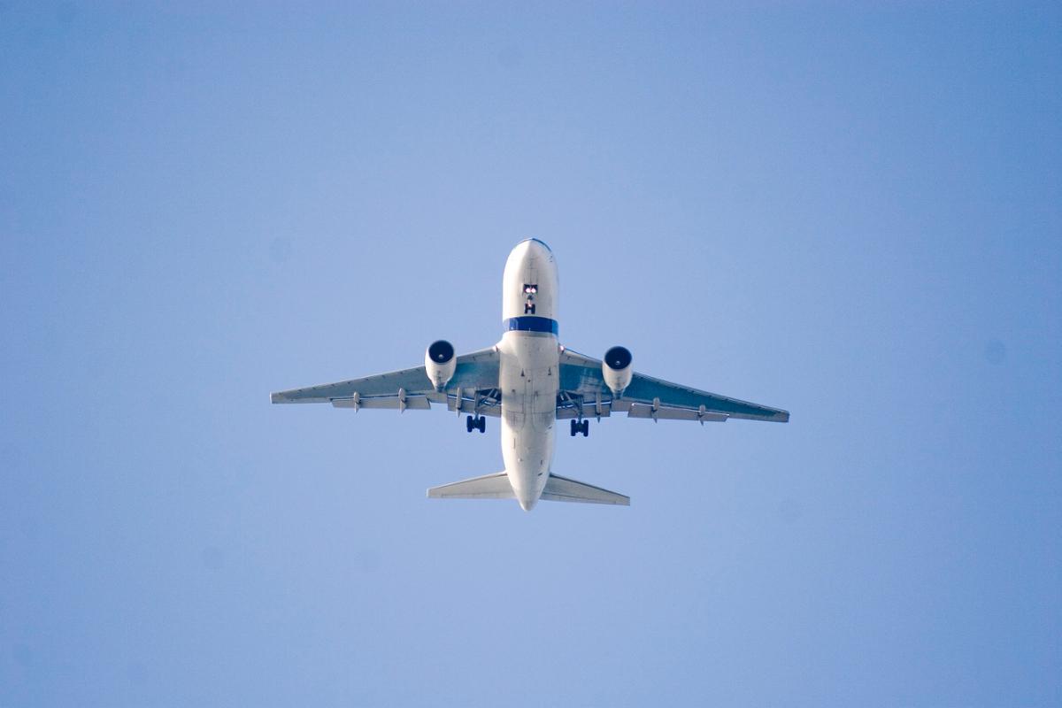 A white airplane flies as seen from below on the ground against a clear blue sky