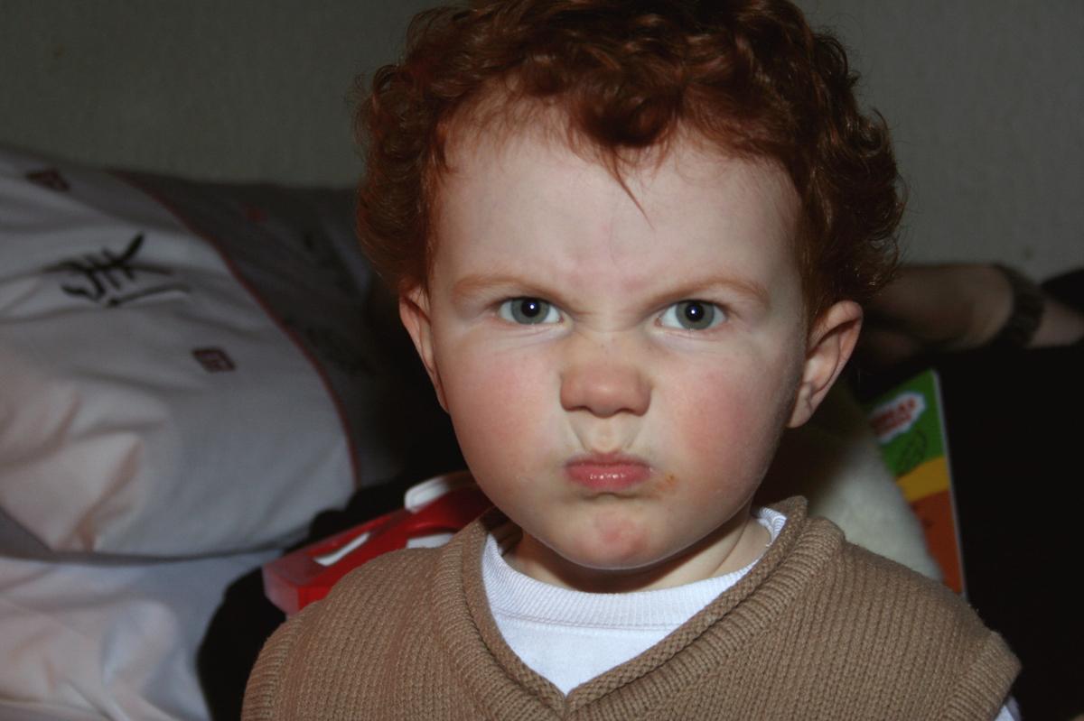 A young child with red hair looks at the camera with an angry face