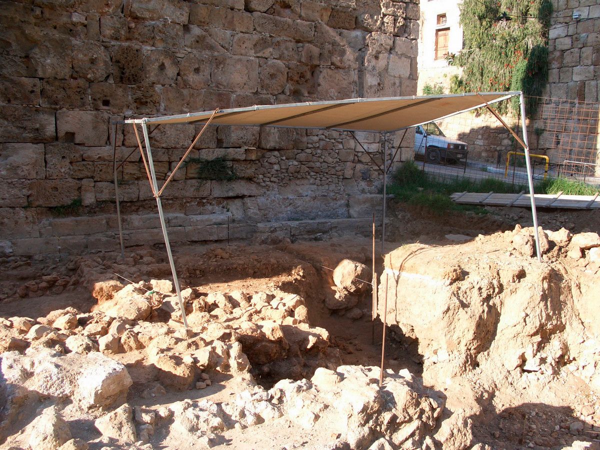 An archaeology dig with a grid laid over holes, with a small canopy above