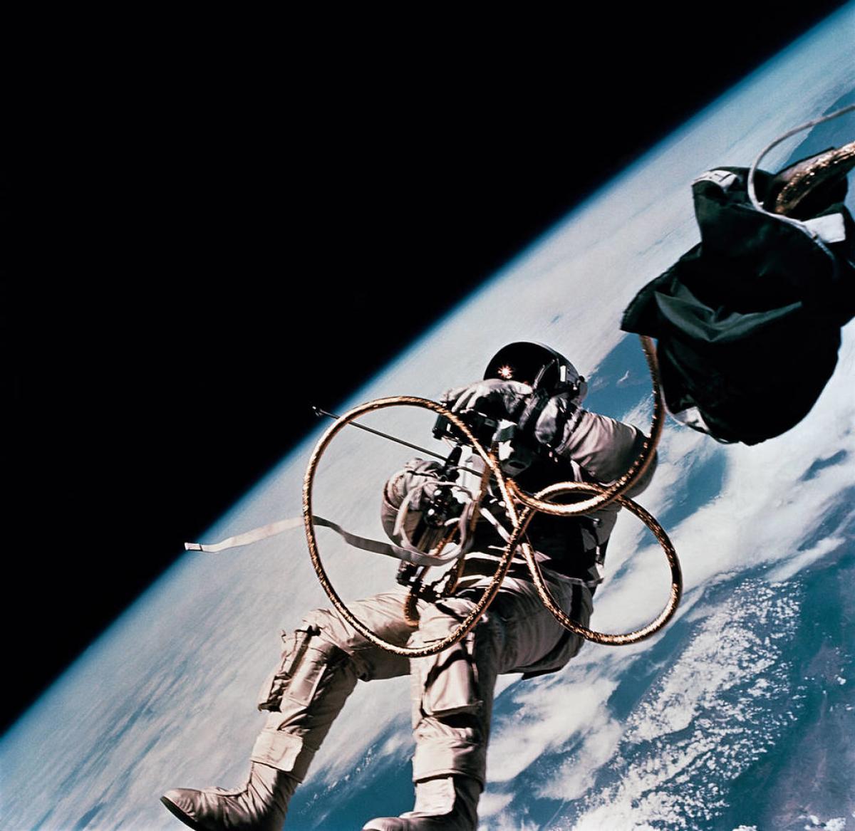 An astronaut floats with a tether in space with Earth seen partially in the background
