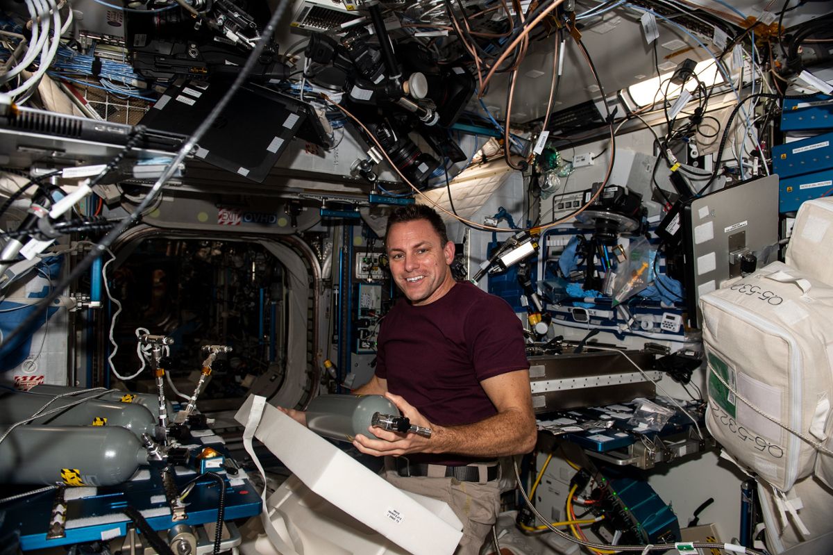 A smiling man replaces bottles while floating inside the International Space Station