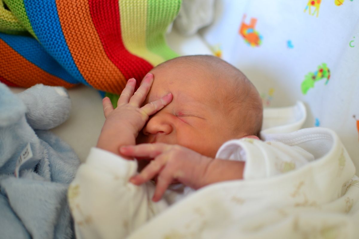 A newborn baby sleeps with both hands close to covering its face