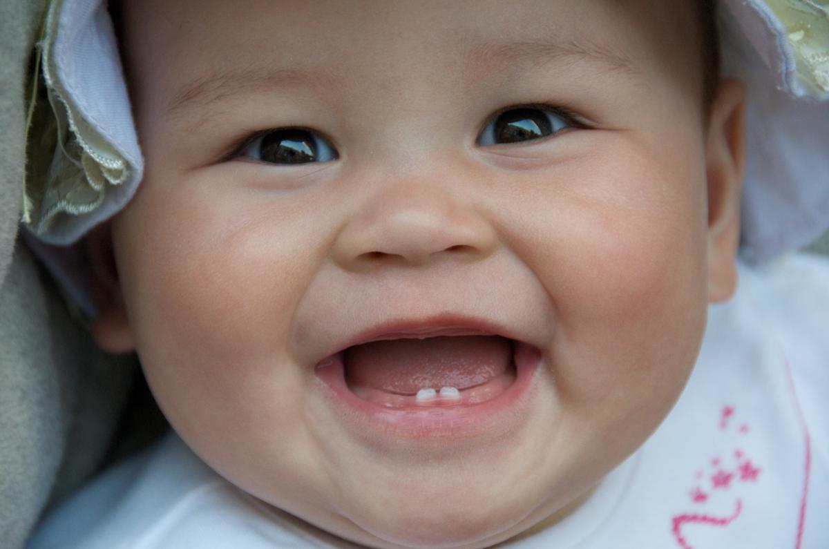 A baby smiles at the camera, showing off two small teeth in their mouth
