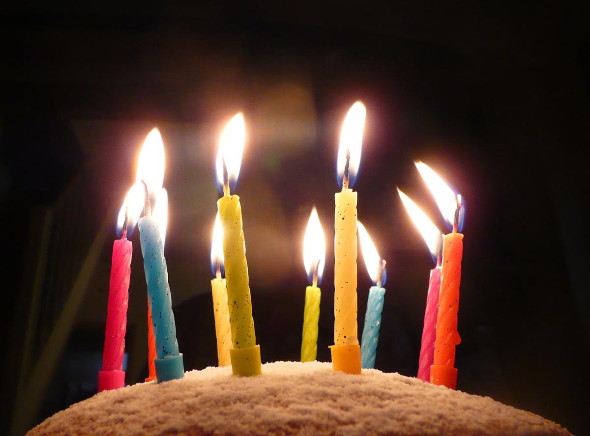 Colorful birthday candles are lit on top of a cake in a dark room, close up