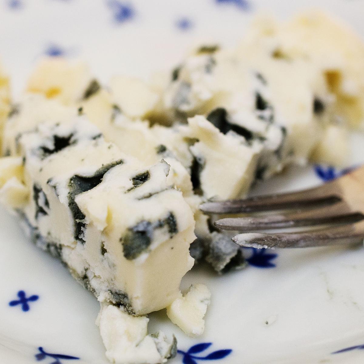 A closeup of blue cheese on a plate with a fork resting next to it
