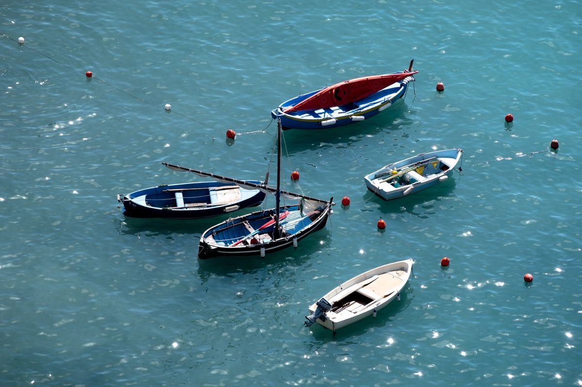 Several small, colorful boats float on clear blue water, with the sun reflecting off the waves