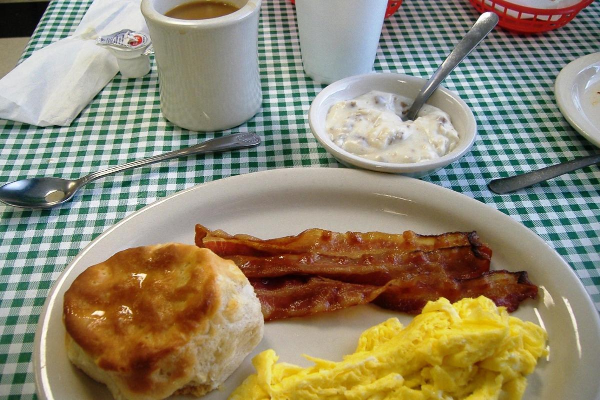 A classic American breakfast with coffee, eggs and bacon and a biscuit on a plate with a blue checkered tablecloth