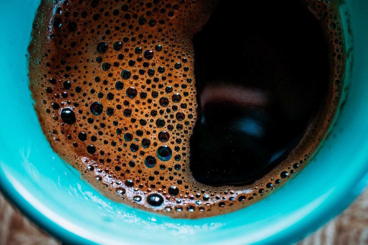 An extreme closeup on a cup of coffee in a blue mug, the coffee with bubbles on the liquid's surface grouped together