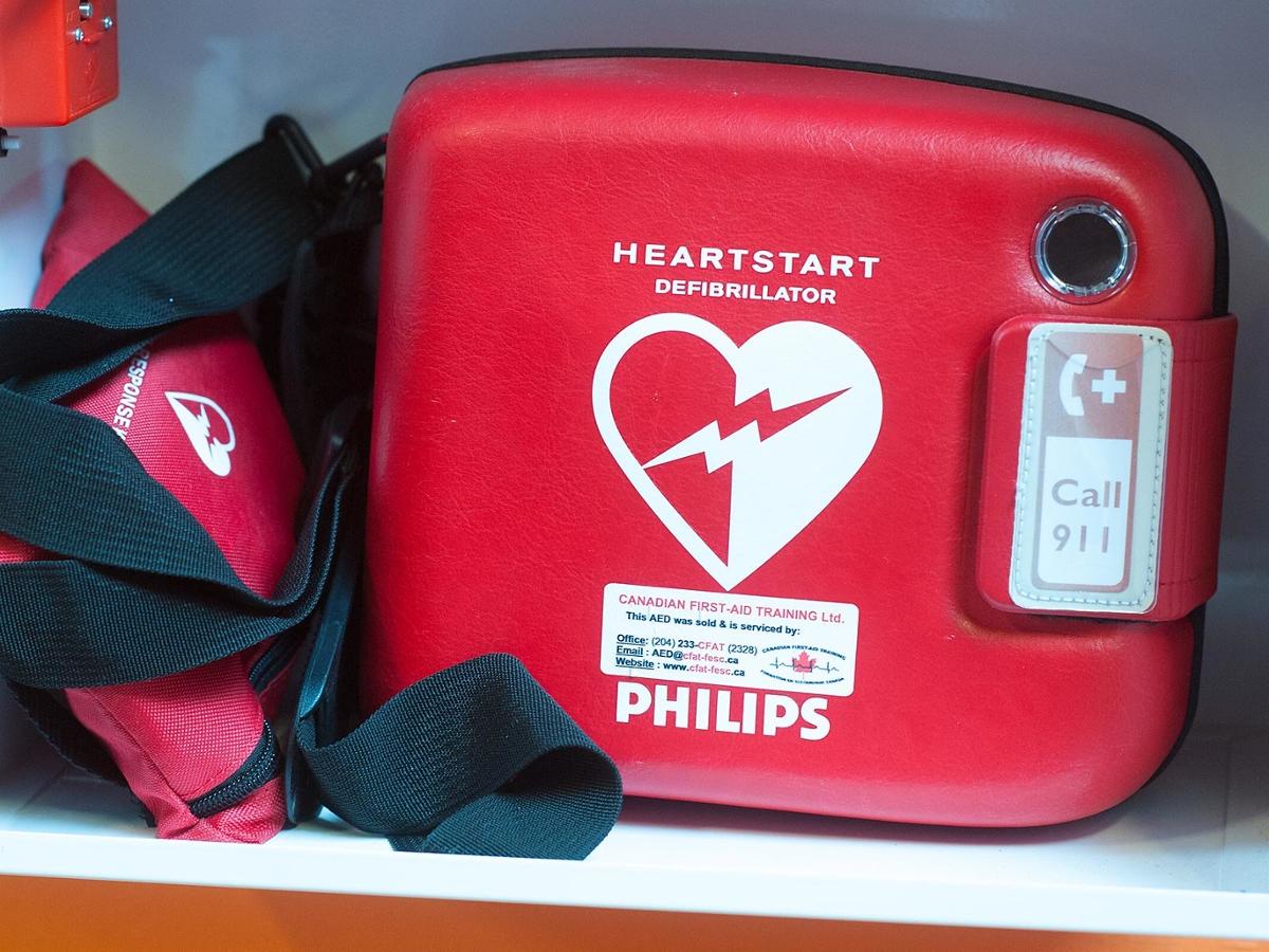 A red defibrillator used in emergency situations sits on a white shelf
