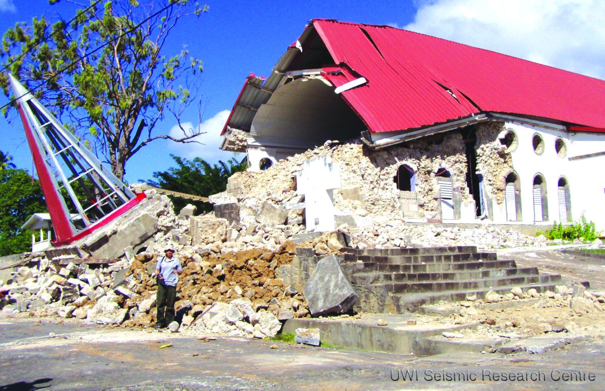 A building half in rubble after an earthquake, with a man standing in front for scale