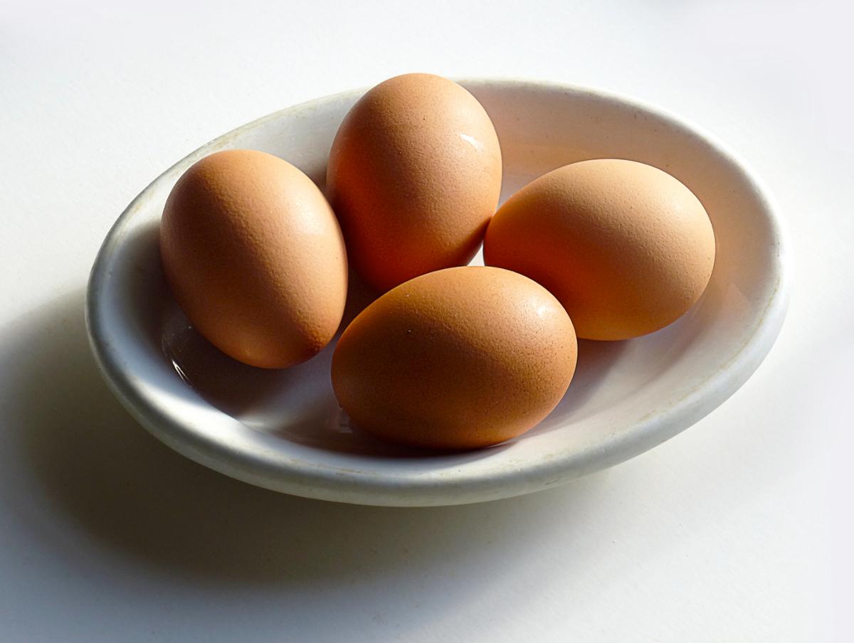 Four brown eggs sit in a small bowl against a white surface
