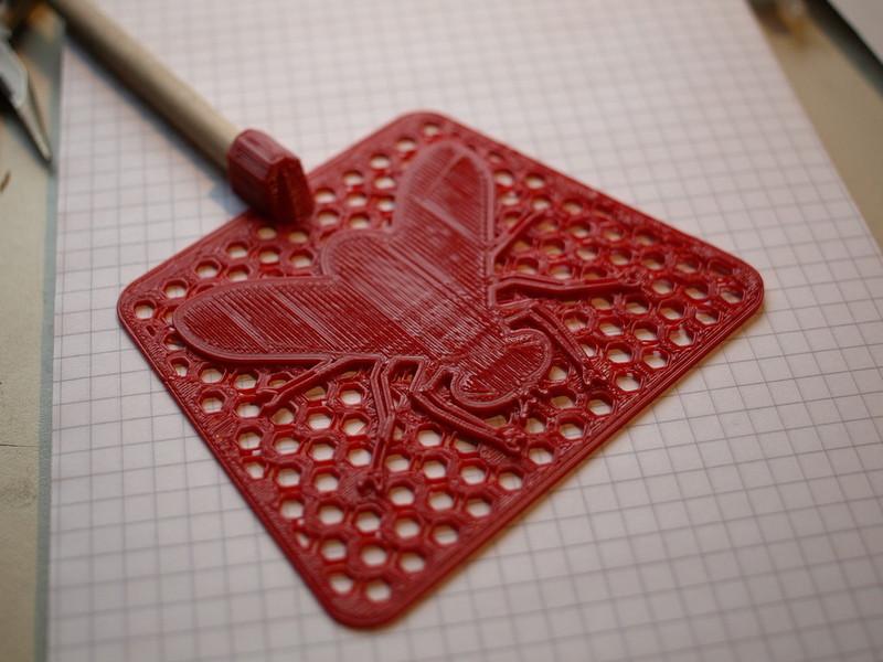 A closeup of a red flyswatter with a fly design on it