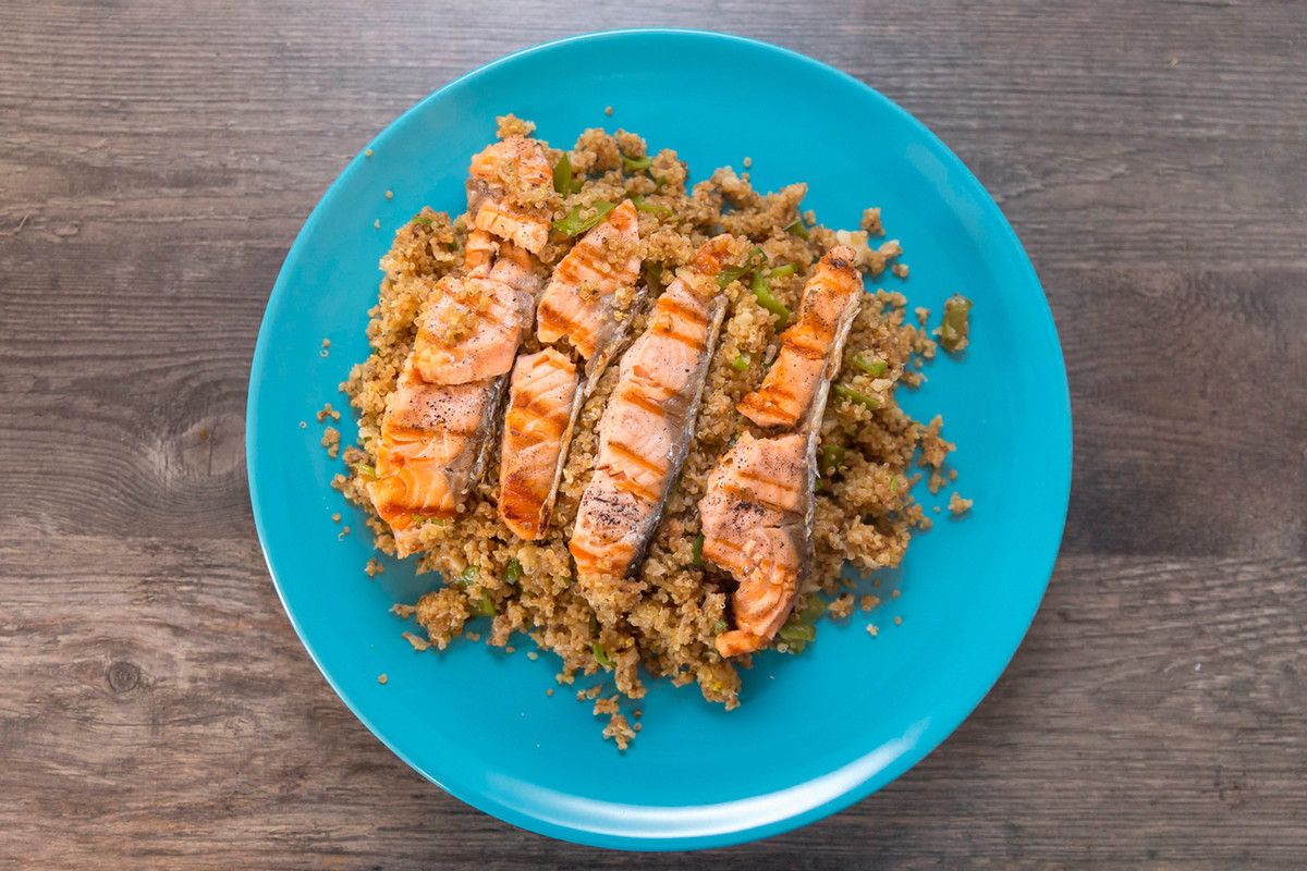 Grilled chicken in strips on top of quinoa, all on a blue plate on a wooden table