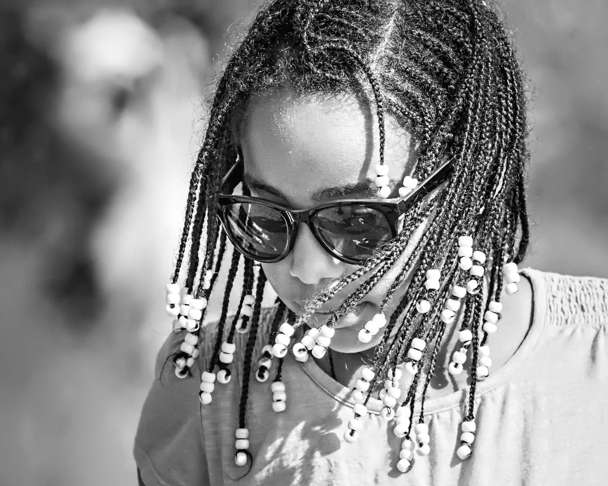 An African American girl with a box braid hairstyle and sunglasses on, in black and white