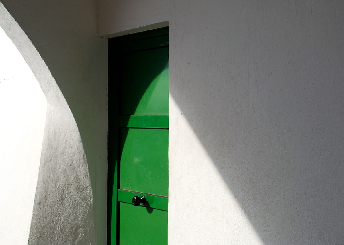 A green door in a beam of sunlight, set in a white wall