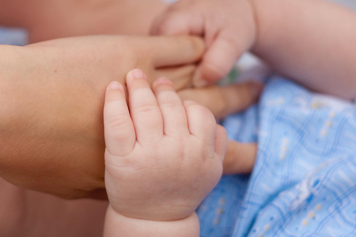 Two baby hands holding on to an adult's hand