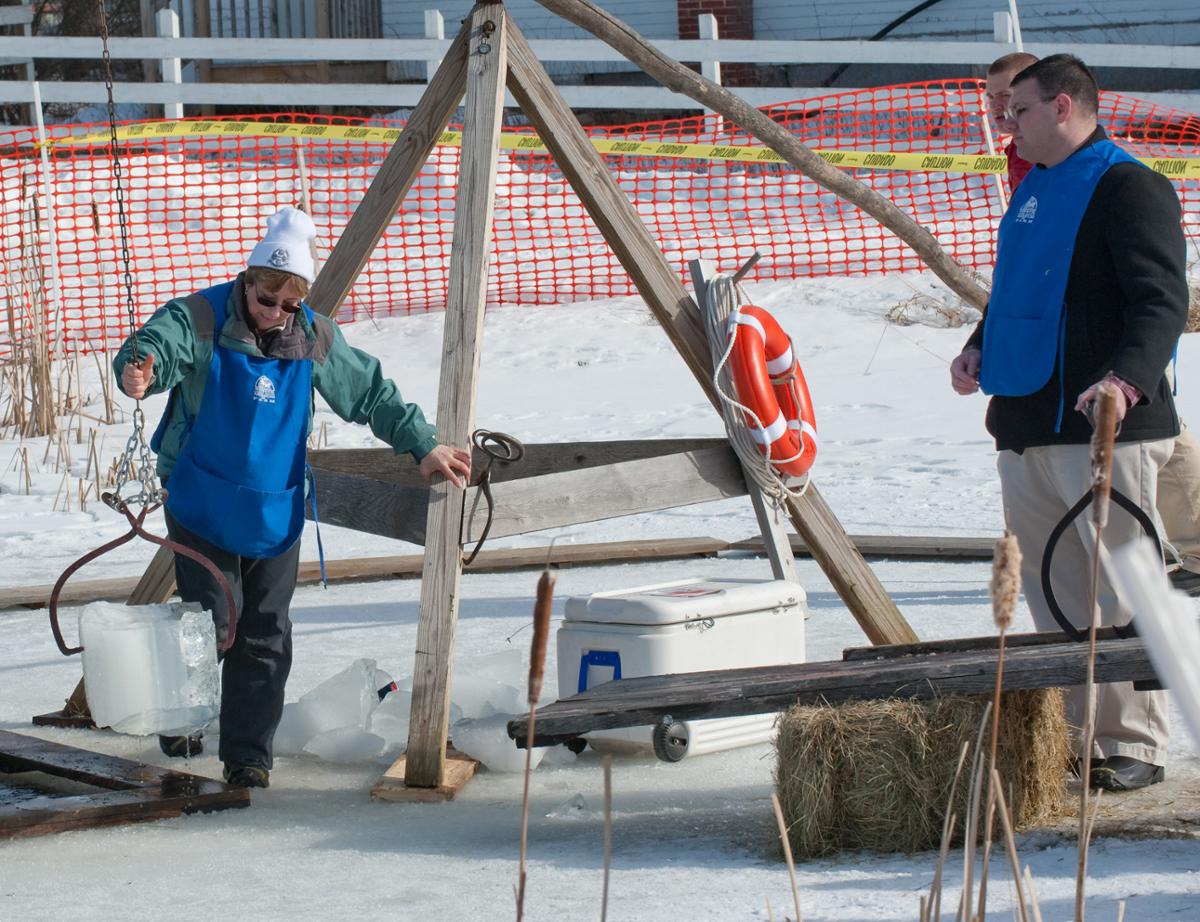 Three people set up a structure to help cut ice blocks out of a frozen pond
