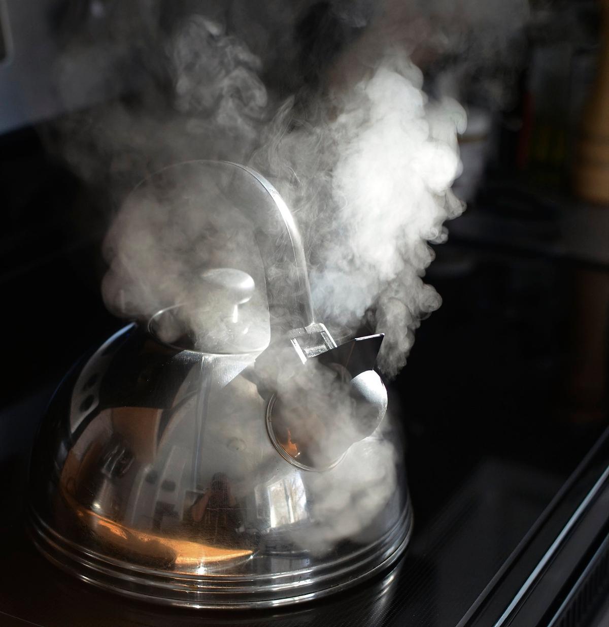 A kettle on a stovetop heating up, with visible steam clouds